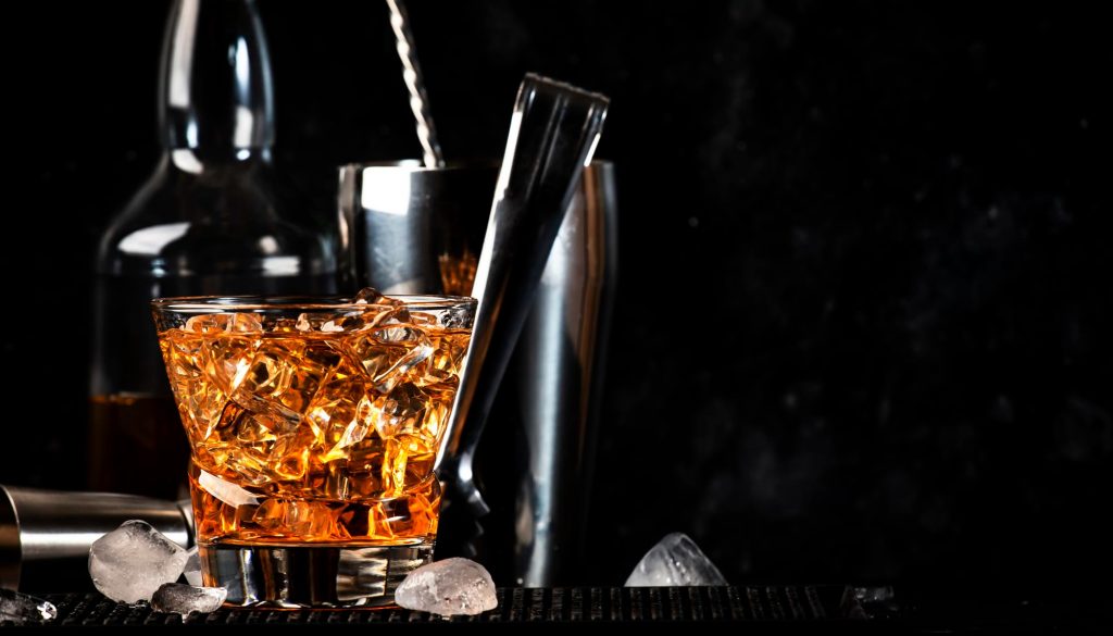 Cocktail Godfather servit într-un pahar old-fashioned pe un fundal negru, cu whisky și amaretto amestecate, evidențiat de o iluminare dramatică.