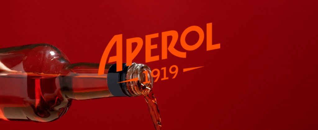 Aperol turnat dintr-o sticlă pe fundal roșu, surprinzând lichidul în mișcare