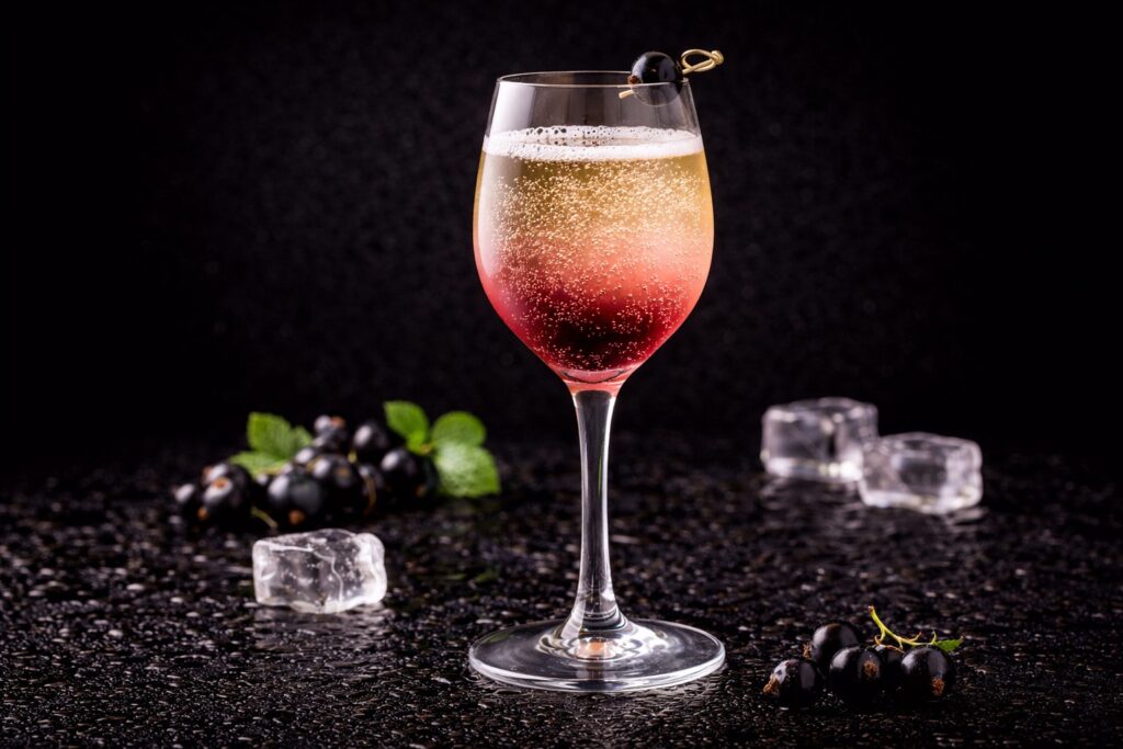 Cocktail Kir în pahar de vin alb cu lichior de coacăze negre și vin alb, fotografiat pe fundal negru elegant.