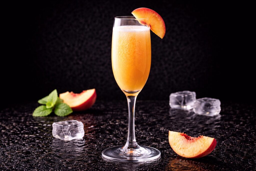 Cocktail Bellini în pahar flute cu piure de piersici și prosecco, decorat cu felie de piersică pe fundal negru.