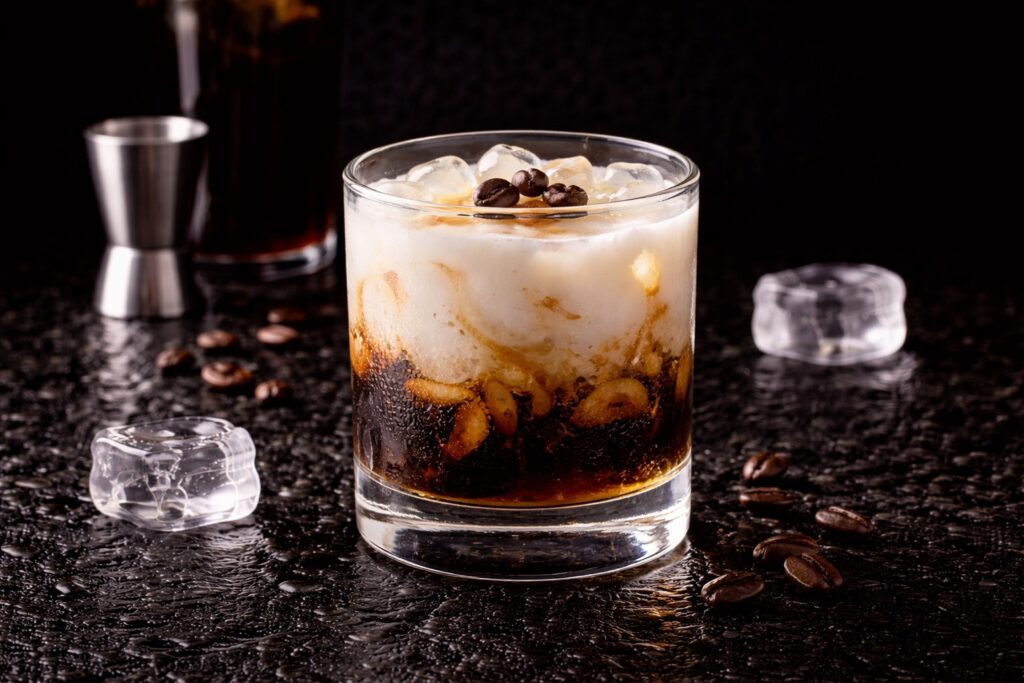 Cocktail White Russian în pahar rocks cu gheață, vodcă, lichior de cafea și smântână, fotografiat pe fundal negru elegant.