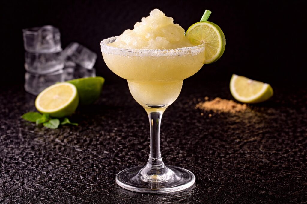 Frozen Margarita în pahar Margarita cu margine de sare, gheață zdrobită și felie de lime, fotografiat pe fundal negru.