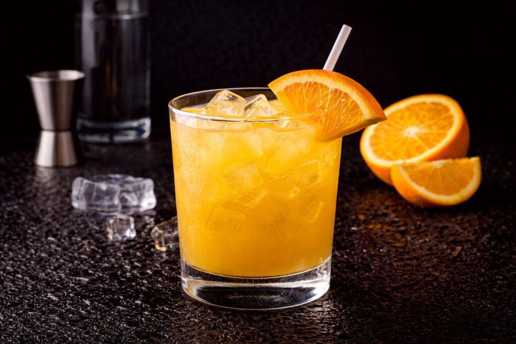 Cocktail Screwdriver în pahar bucket cu gheață, vodcă și suc de portocale, decorat cu felie de portocală pe fundal negru.