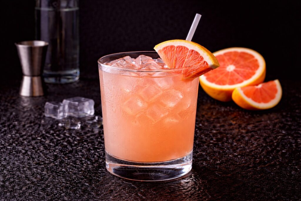 Cocktail Greyhound în pahar bucket cu gheață, vodcă și suc de grapefruit, decorat cu felie de grapefruit pe fundal negru.