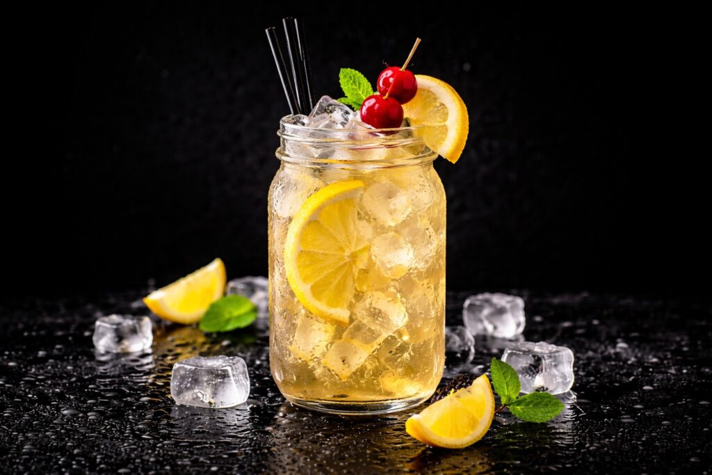 Cocktail Lynchburg Lemonade în pahar mason jar cu cuburi de gheață, felie de lămâie și cireșe, fotografiat pe fundal negru elegant.