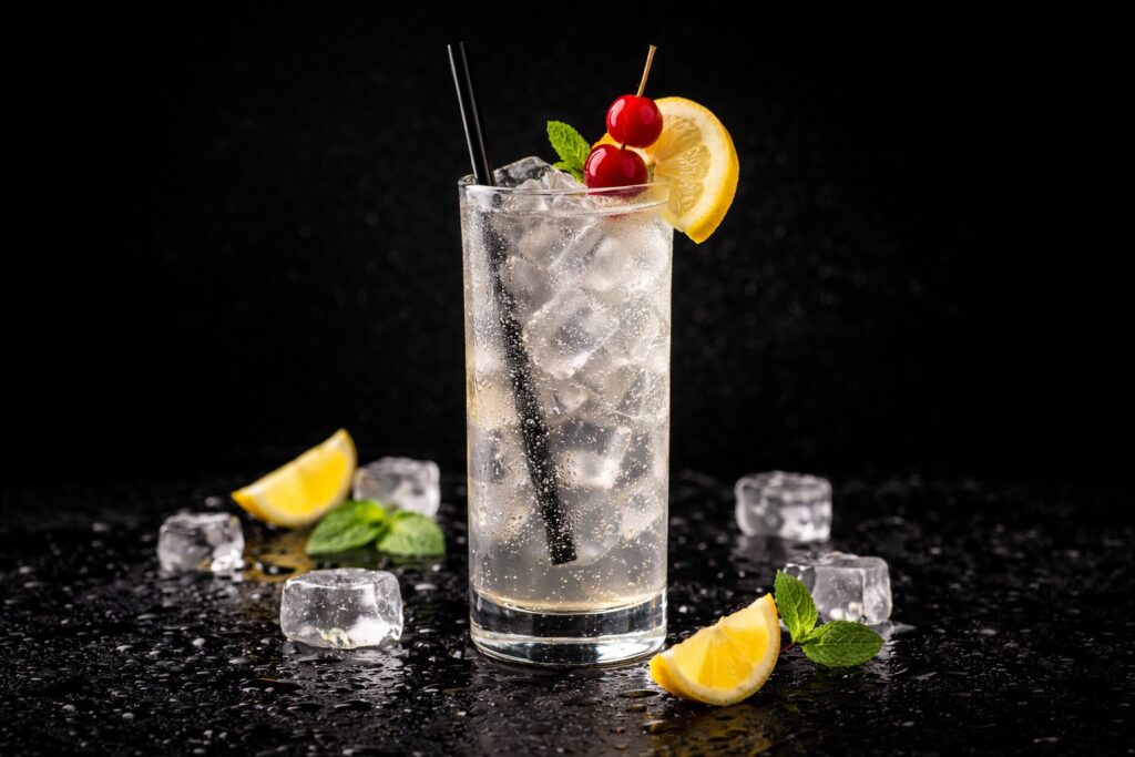 Cocktail Tom Collins în pahar Collins cu cuburi de gheață, felie de lămâie și cireșe, fotografiat pe fundal negru elegant.