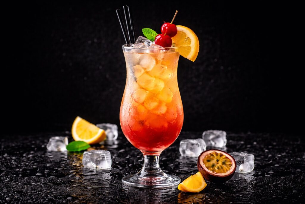 Cocktail Hurricane în pahar hurricane cu cuburi de gheață, gradient roșu-portocaliu, decorat cu portocală și cireșe, pe fundal negru elegant.