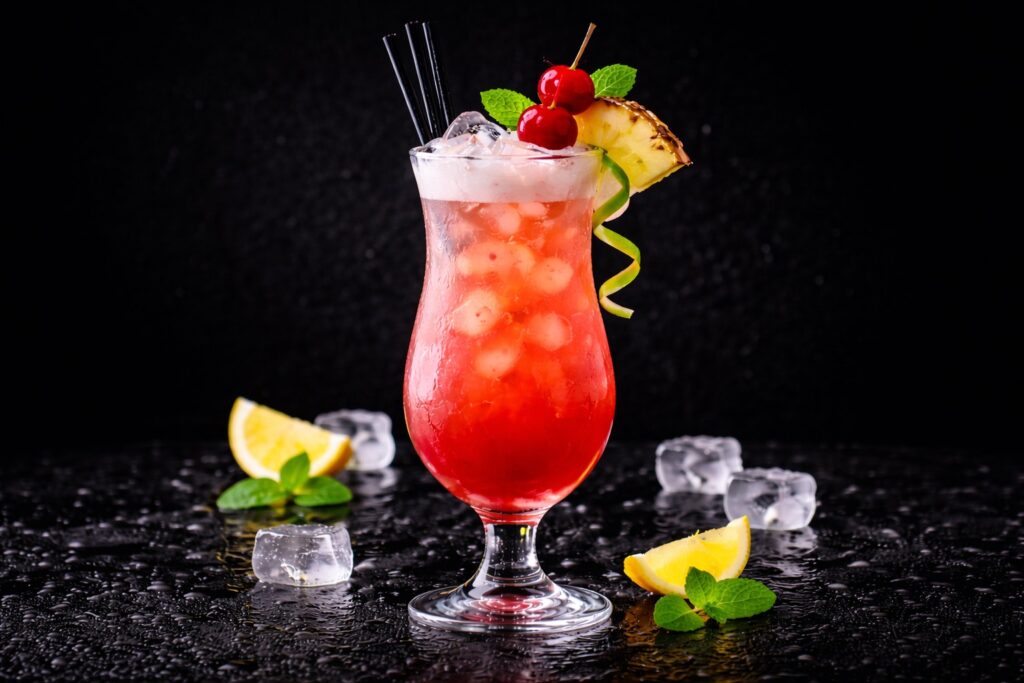 Cocktail Singapore Sling în pahar hurricane cu gheață, culoare roz-roșie, decorat cu ananas, cireșe și mentă pe fundal negru elegant.
